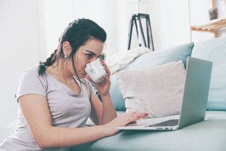 年轻女人使用笔记本电脑，在家里喝咖啡