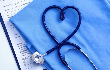 医用听诊器扭曲心形躺在病人医疗历史记录列表和蓝色医生统一特写。医疗帮助或保险的概念。心脏病学护理 保健 保护及预防