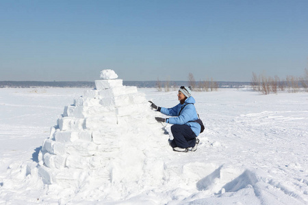 妇女在蓝色夹克建立一个冰屋在雪空地上