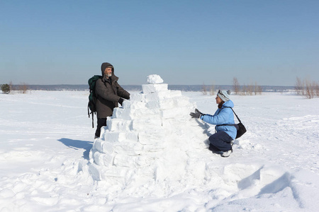 在冬天的雪林中, 男人和女人在雪地上建造一座冰屋。