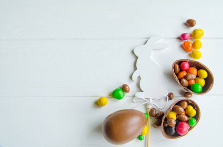 与巧克力蛋和糖果白色木制背景上的白色复活节兔子