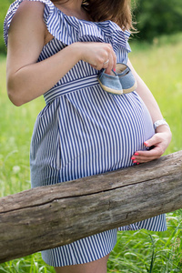 孕妇肚子抱着期待的女孩的蓝色婴儿鞋