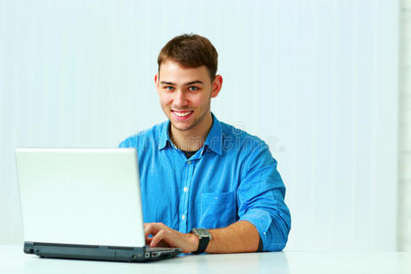 微笑的年轻商人在笔记本电脑上打字，看着相机