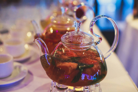 美丽温暖的图片的透明茶壶水壶与苹果 柠檬和姜蜡烛与甜点在背景中的桌上美味绿色红茶