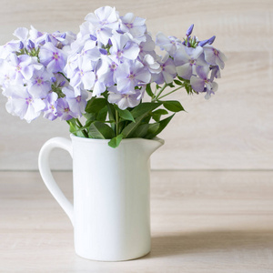 在木制的背景上有一个白色花瓶蓝夹竹桃的花束