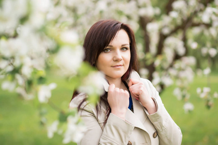 美丽年轻的黑发女人站附近花朵盛开的苹果树在温暖的春日
