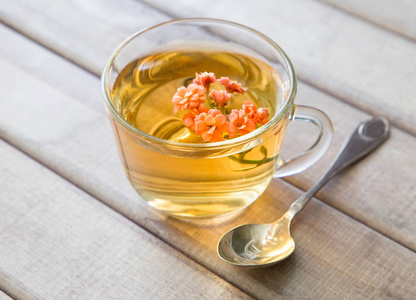 特写镜头的杯茶，鲜艳的花朵，用勺子木制的桌子上。静物与茶杯