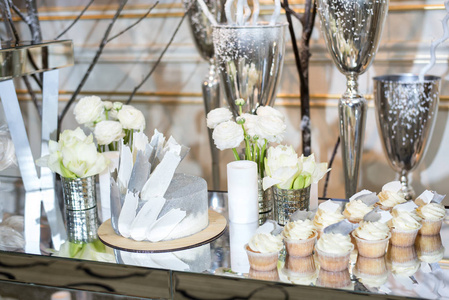 婚礼蛋糕和纸杯蛋糕桌上的装饰着白色的鲜花和蜡烛和花瓶