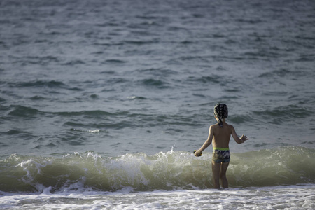 一个男孩在海滩上玩海水和挥手致意