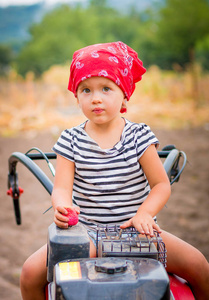 红头巾和条纹 t 恤的孩子坐在舵柄在球场上。宝贝女孩司机修炼