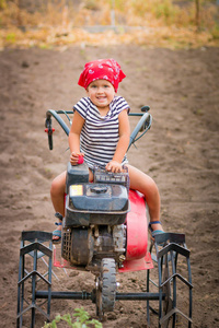 快乐的孩子，在红色的头巾和条纹 t 恤坐在舵柄在球场上。宝贝女孩司机修炼