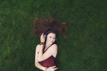 年轻漂亮的女孩躺在草地上的耳机听音乐