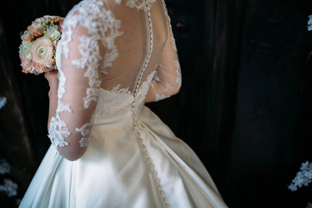 新娘穿着一件白色的连衣裙她背转身，她捧着婚礼花束
