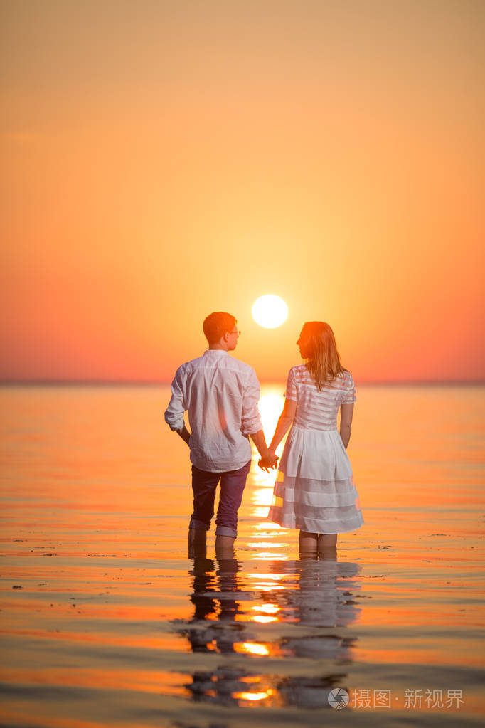恩爱的夫妻在日落时在水中