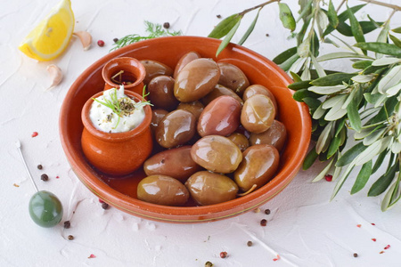 在传统的棕色陶瓷碗，用酸奶汁酱 柠檬 大蒜，橄榄橄榄枝和橄榄油在一张白纸抽象背景