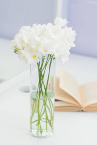束白色鲜花插在花瓶里放一张桌子。舒适的图片。花瓶和白色的桌上一本书中的白色花束