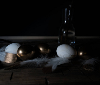 复活节。复活节的夜晚。金色和白色鸡蛋，一张木桌上的羽毛。复古。黑暗的背景