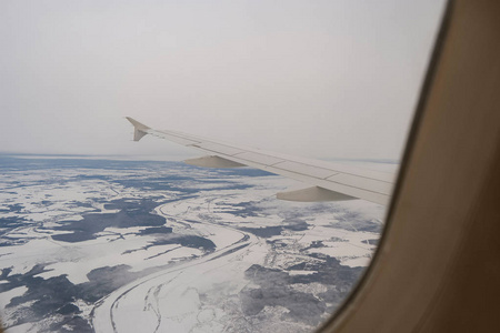 带着雪在陆地上空飞行。客机翼和冬季景观之下