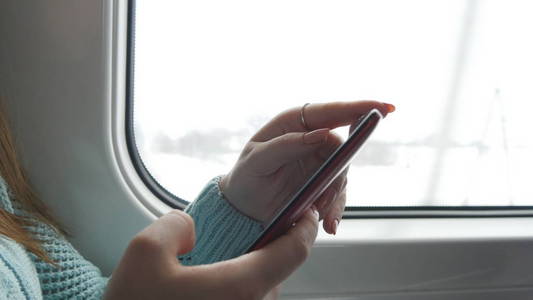 年轻女子在一辆火车旅行和使用手机。女手从智能手机发送消息。和朋友聊天的女孩的手臂。关闭
