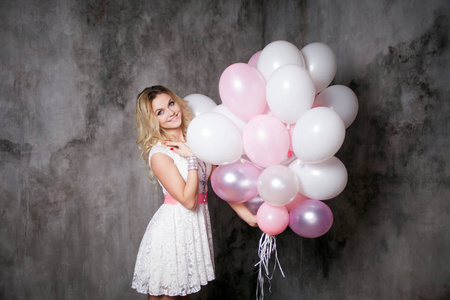 迷人的年轻金发女郎穿着白色与粉红色的腰带，举行党的一大捆的气球
