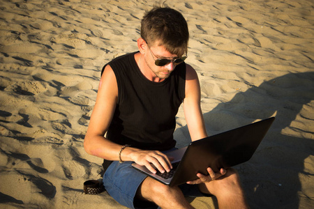 年轻人正在海滩上的手提电脑。减档