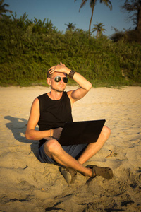 年轻人正在海滩上的手提电脑。减档