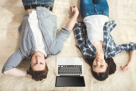夫妇躺在地毯上之间的笔记本电脑