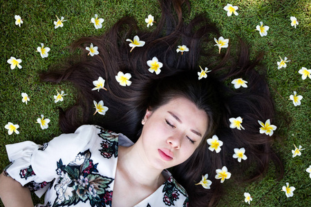 亚洲美丽的年轻女子躺在草坪上用鲜花