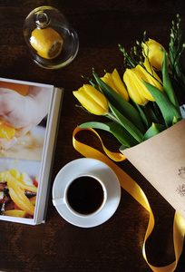 一杯黑咖啡和一束黄色郁金香在牛皮纸在桌子上。预订与明亮的图片