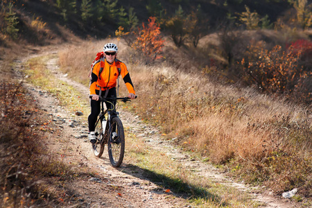 橙色的夹克衫，日出时在农村公路上骑自行车的自行车手