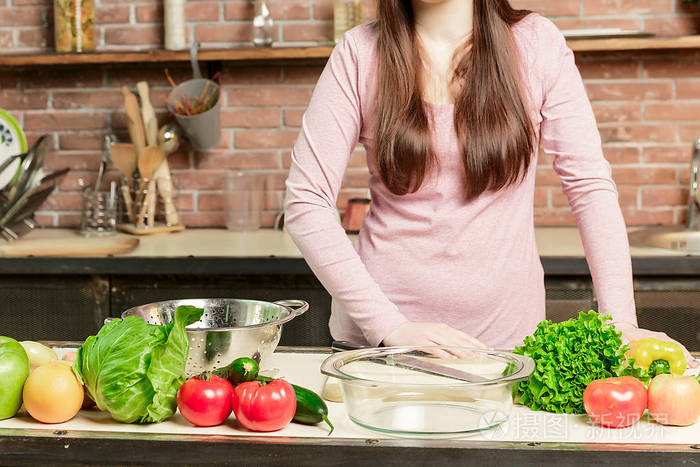 年轻的女人在家里的厨房里做饭健康的食物饮食节食的概念健康的生活