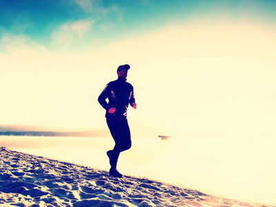 轮廓的运动积极的人在日出时在湖滩上运行。健康的生活方式