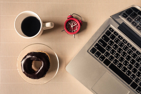 咖啡杯 甜甜圈和时钟的笔记本电脑桌上的顶视图