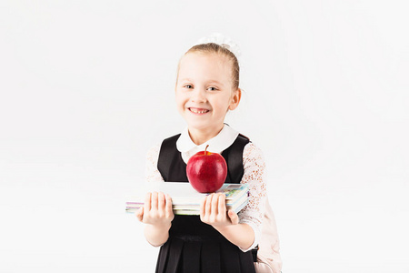 读书的孩子。 微笑的小女孩带着大背包，拿着书，大红苹果在白色的背景下。 看着摄像机。 学校观念。 回到学校