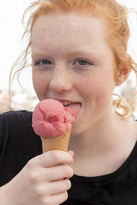 年轻小姐舔粉红色冰淇淋锥直接凝视