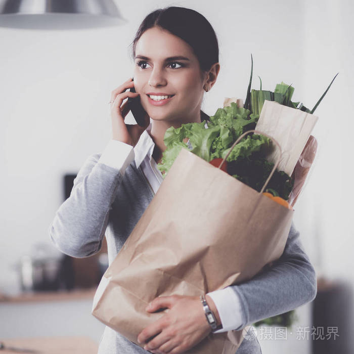 年轻女子捧着蔬菜杂货店购物袋。站在厨房