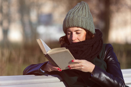 一个戴着帽子的女孩坐在公园长凳上和看书