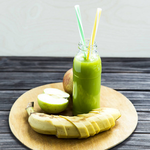 苹果弯的管从原始的苹果和香蕉,黄色和绿色的管透明瓶新鲜果汁照片