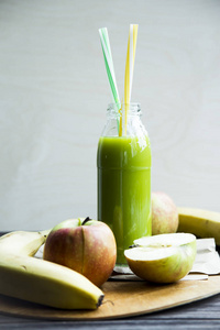 从原始的苹果和香蕉,黄色和绿色的管透明瓶新鲜果汁照片