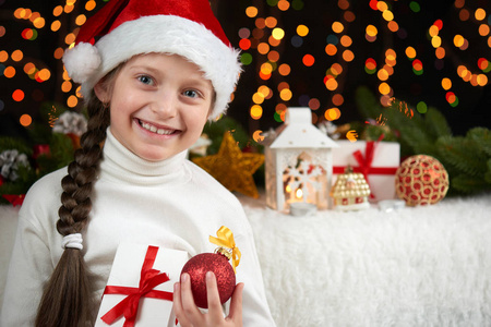 在黑暗的背景，与圣诞装饰 面部表情和快乐的情绪，孩子女孩画像穿着圣诞老人的帽子，冬天假日概念