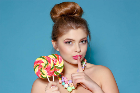 一个美丽的年轻女子用糖果在蓝色背景上的肖像。金发女郎，有着彩色的糖果。甜甜。聪明的女人