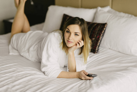 美丽的女人躺在床上和在酒店房间看电视照片