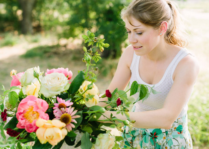 花束，人和插花概念   年轻女人做束美丽的粉红牡丹 玫瑰 康乃馨和雏菊，在工作与花在花园里的白色连衣裙的女孩花店