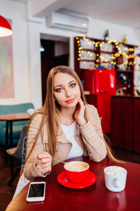 美丽的年轻女子在一家咖啡馆的咖啡红杯。女人在舒适的咖啡厅喝热咖啡