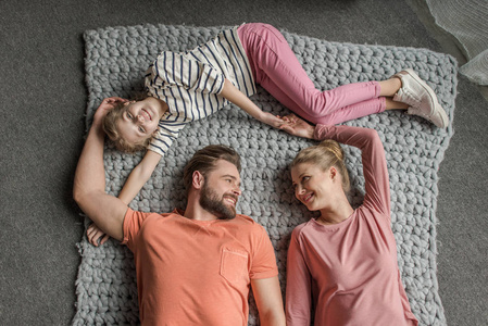 顶视图的幸福的家庭，有一个孩子在灰色针织地毯上躺在一起
