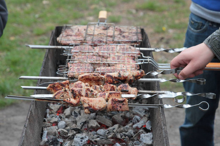 用串煮肉。人的手把烤肉放在马甲上。烹饪野餐食品