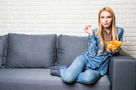 年轻女子看电视，在沙发上吃薯片