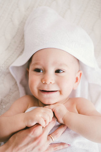 美丽微笑的初生男婴长满了白色竹毛巾与乐趣的耳朵。躺在白色的针织 羊毛格子明亮室内。妈妈的手是对孩子。自然光线