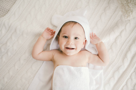 美丽微笑的初生男婴长满了白色竹毛巾与乐趣的耳朵。坐在白色的针织 羊毛格子明亮室内。窗口的轻