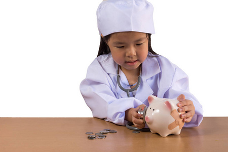 亚洲女孩扮演医生照料储钱罐，孤立的背景